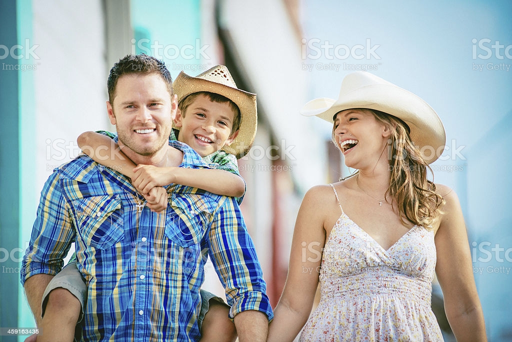 Boy in cowboy hat getting piggyback ride from dad as mom looks on and laughs.