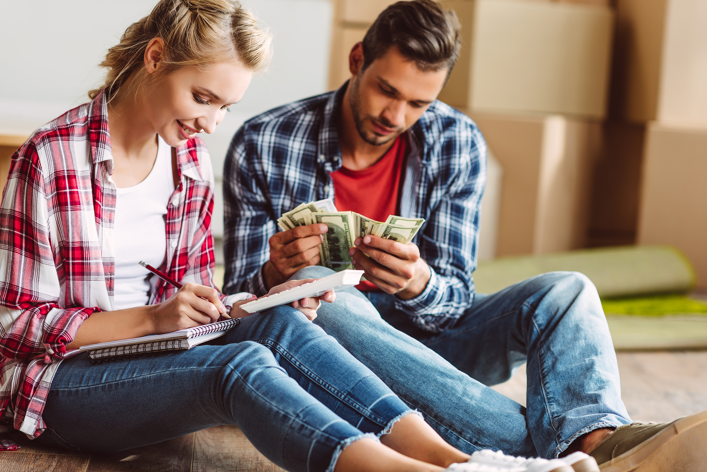 young couple counting money while sitting on floor in new home