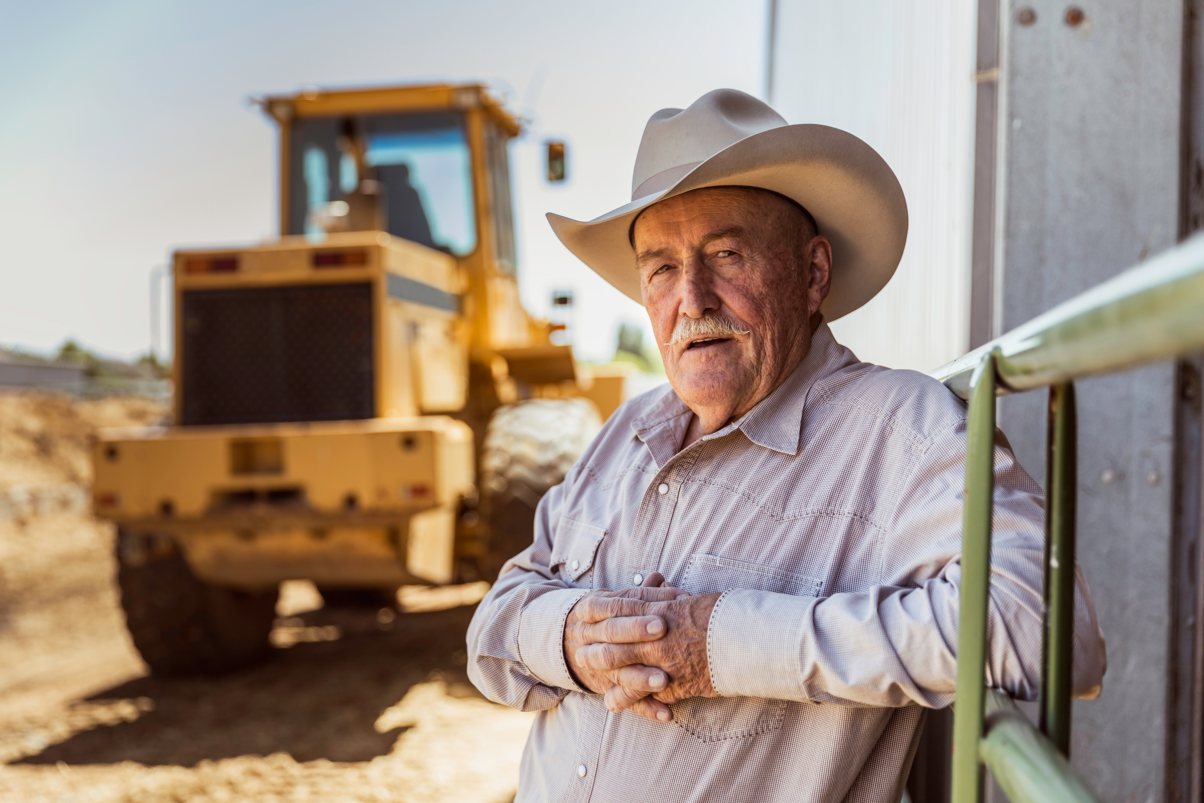 Mature farmer with equipment behind him and looking at camera
