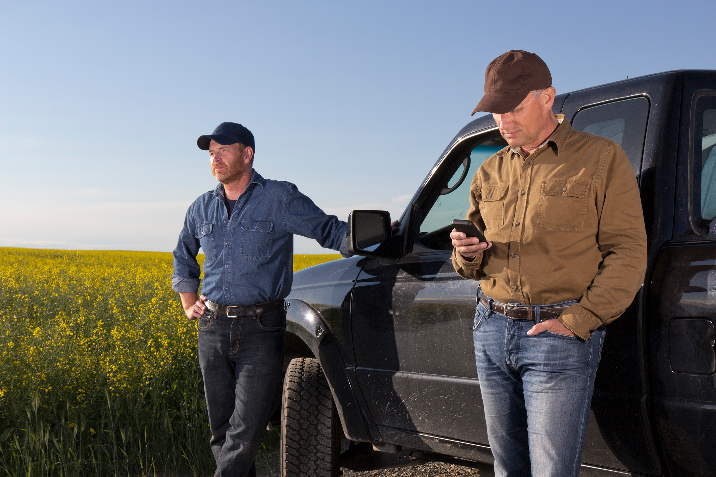 Two farmers standing in field next to truck and one looking at smartphone
