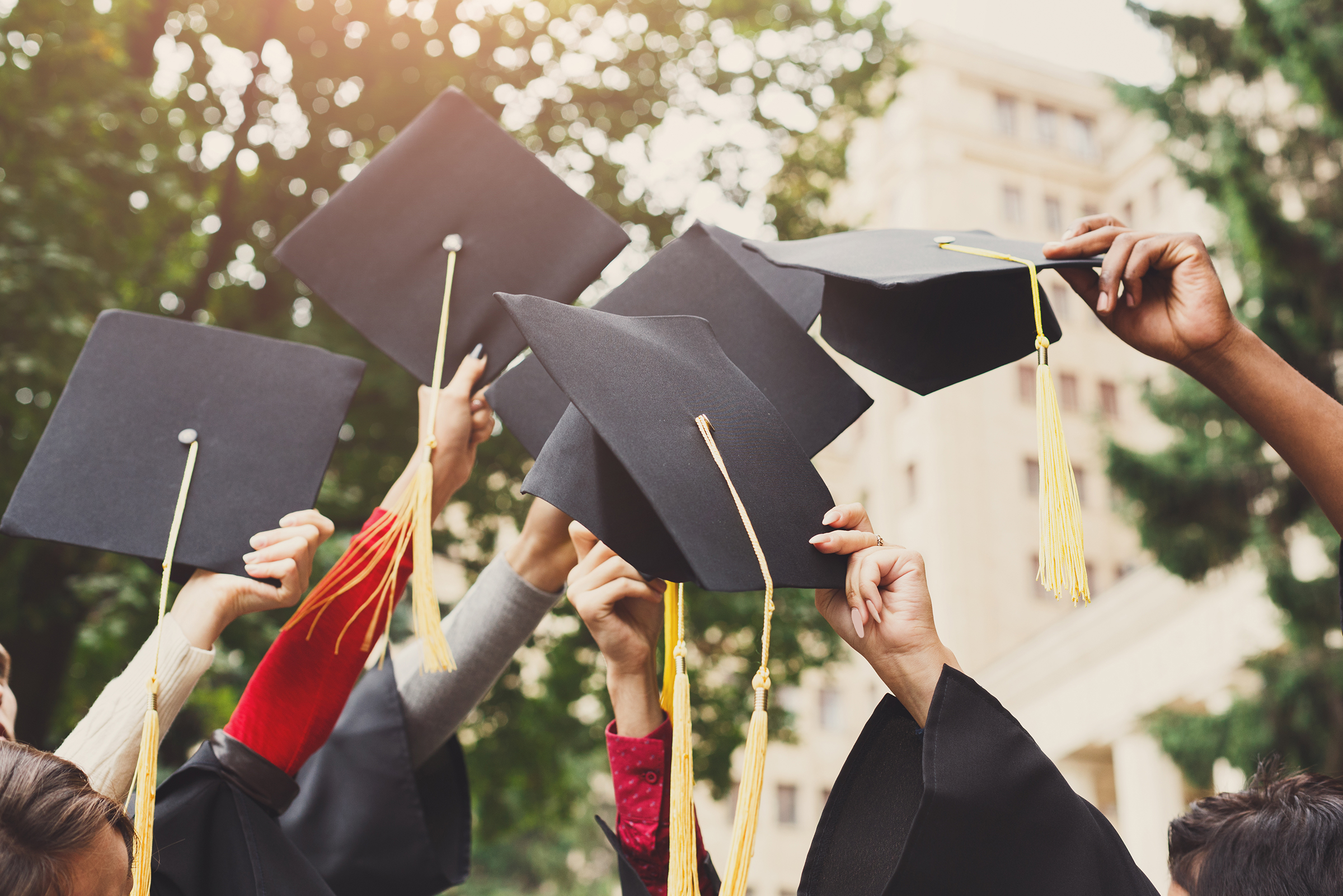 A group of multi ethnic students celebrating their graduation by throwing caps in the air closeup.