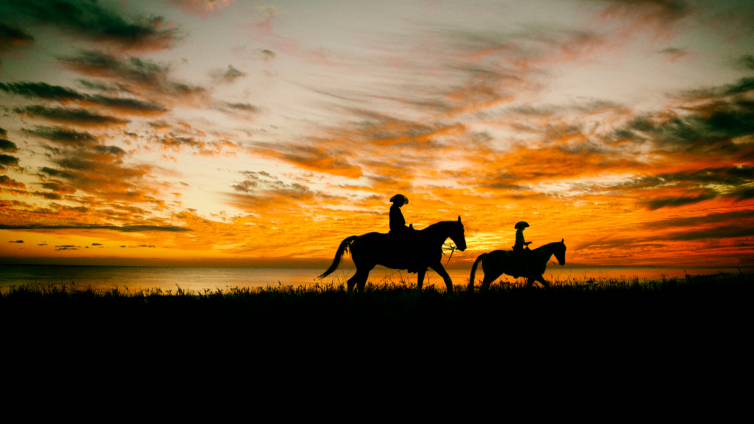 Mother and daughter on horseback in a field with as sunset.