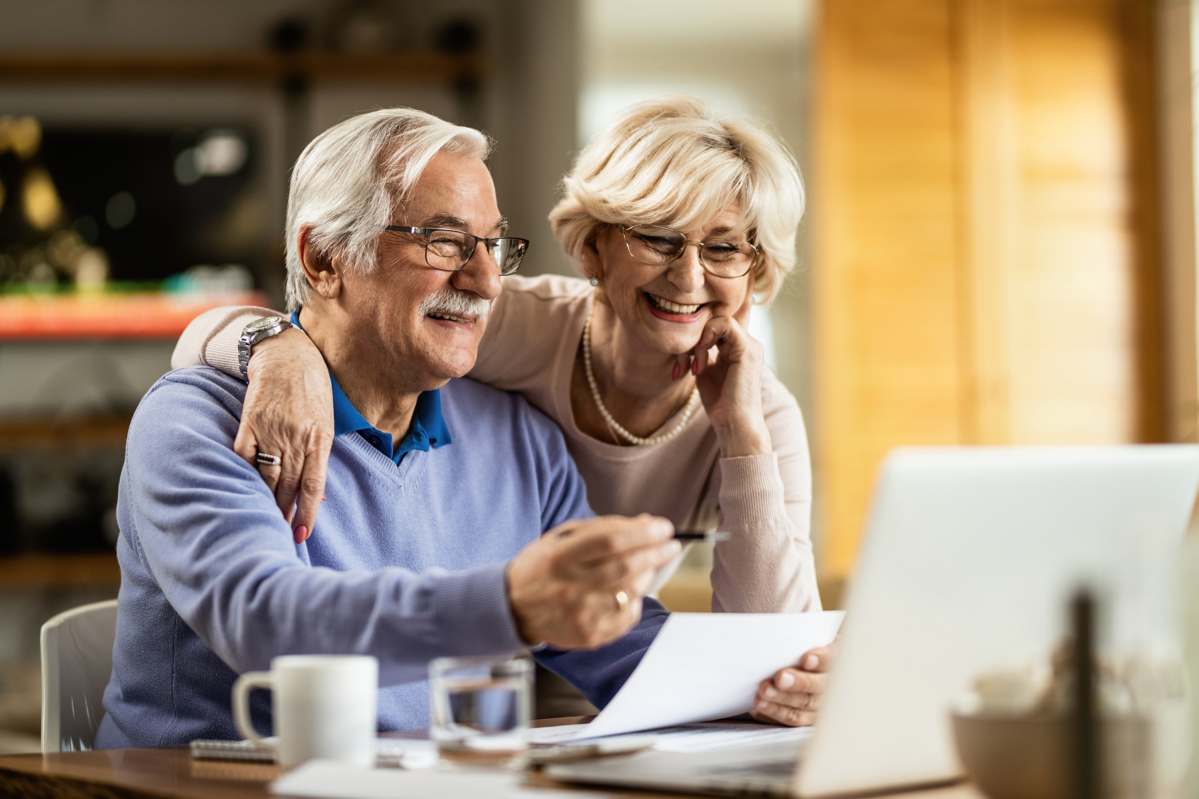 Happy senior couple going through home finances and using computer at home.