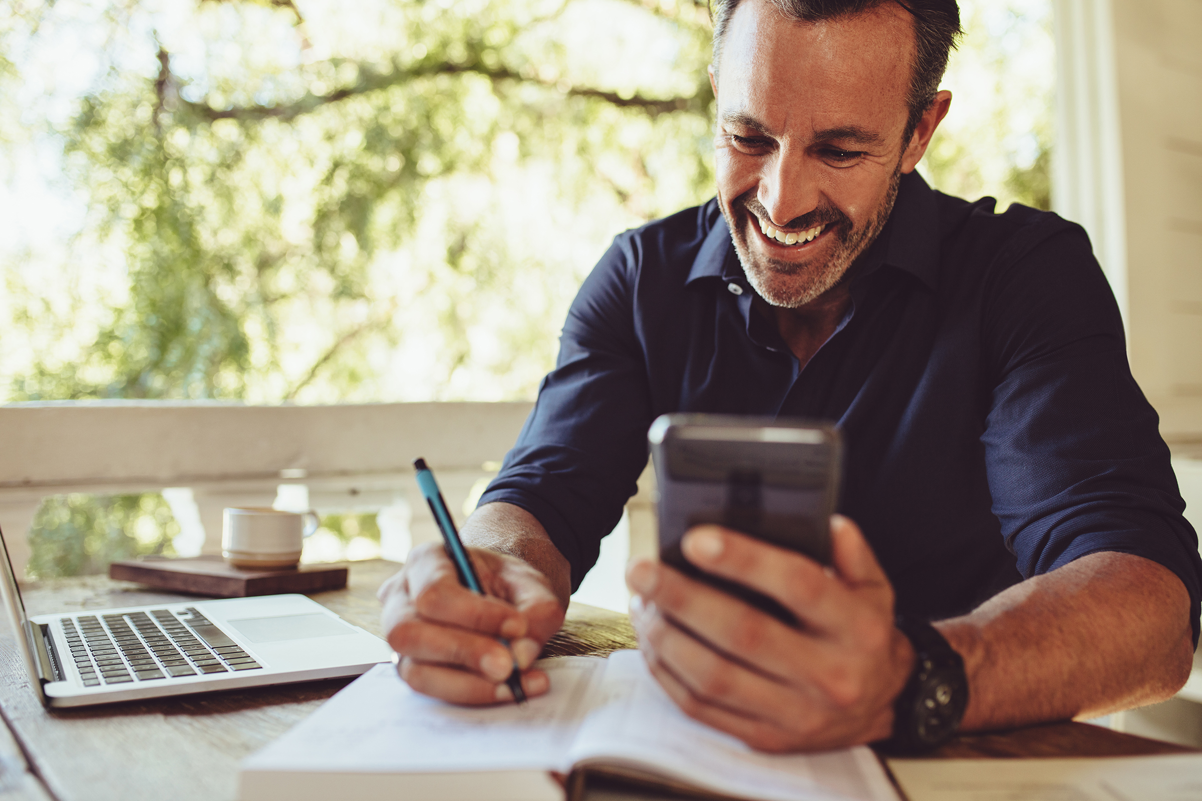 Smiling man sitting at table with laptop computer and smartphone.