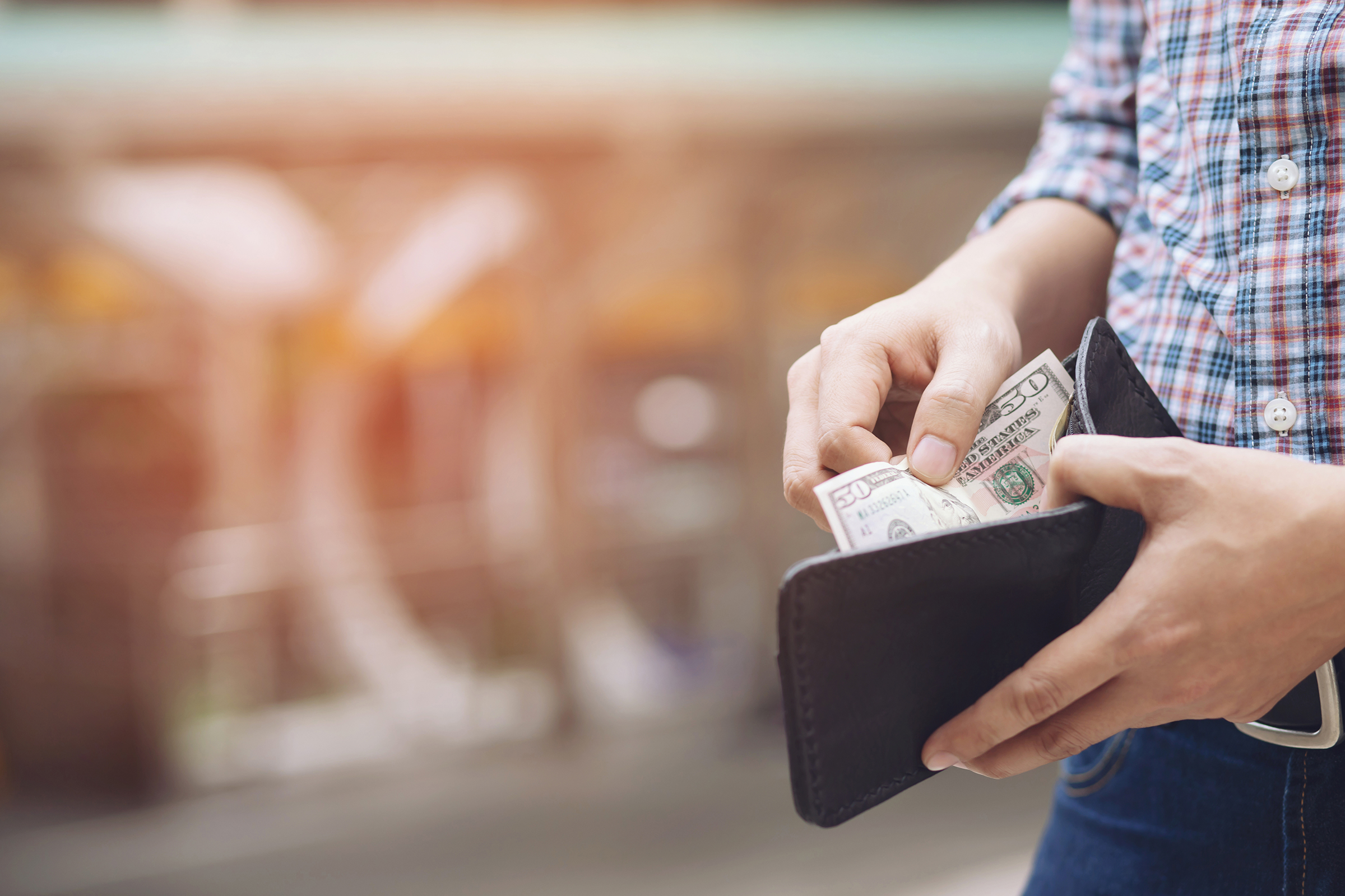 Man with plaid shirt opening wallet to remove cash.