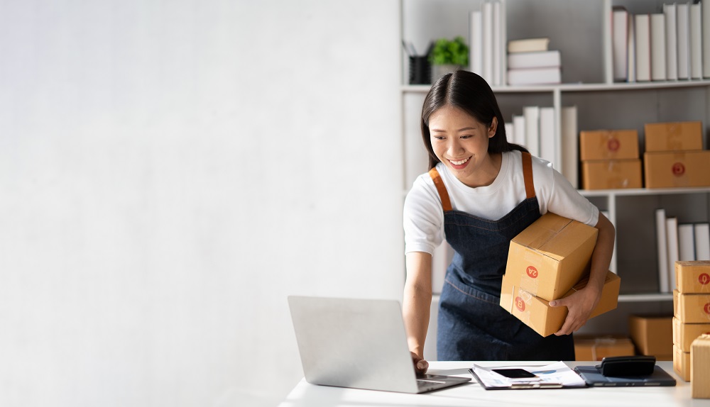 Woman typing on a laptop holding boxes