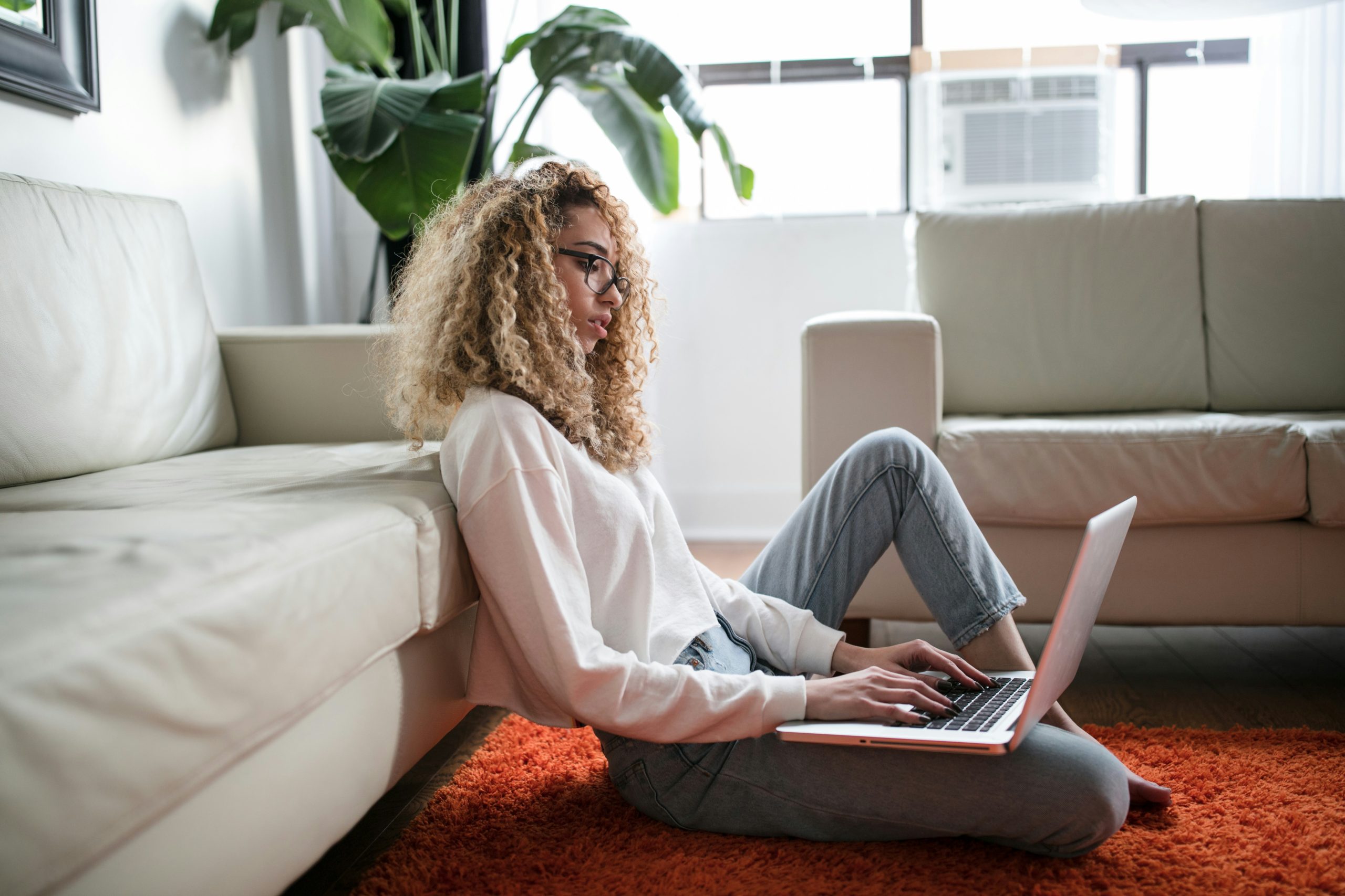 Woman sitting on the floor in front of a couch typing on a laptop