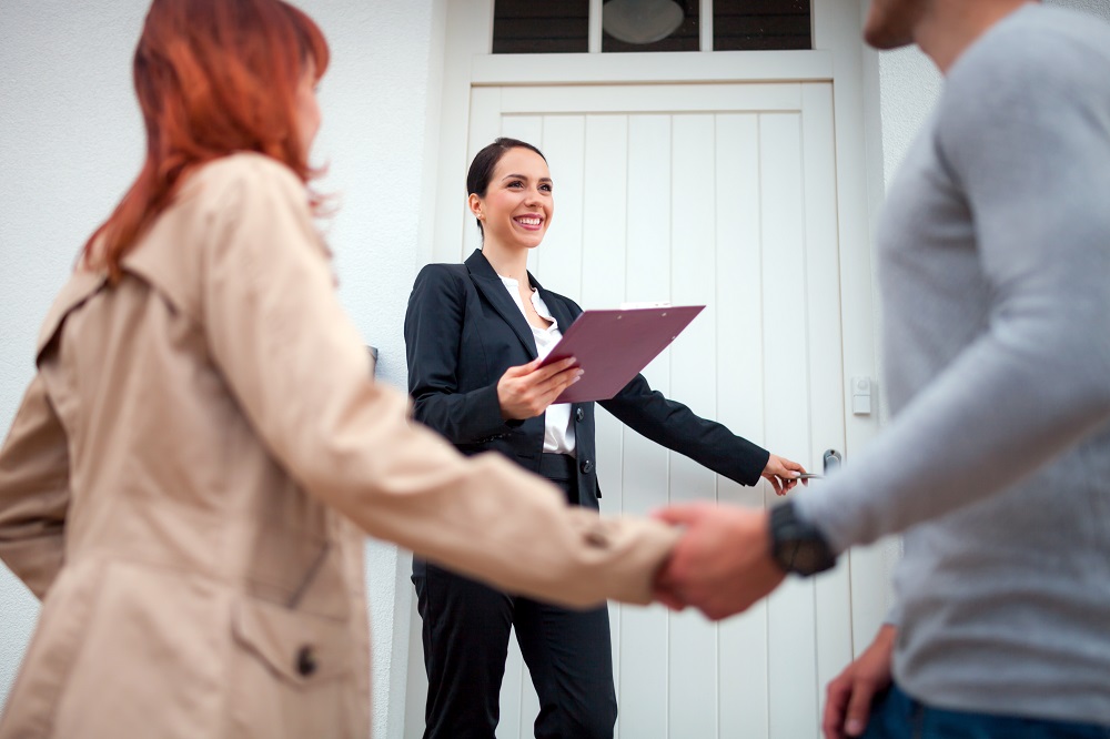 Real estate agent near door inviting young couple to enter house