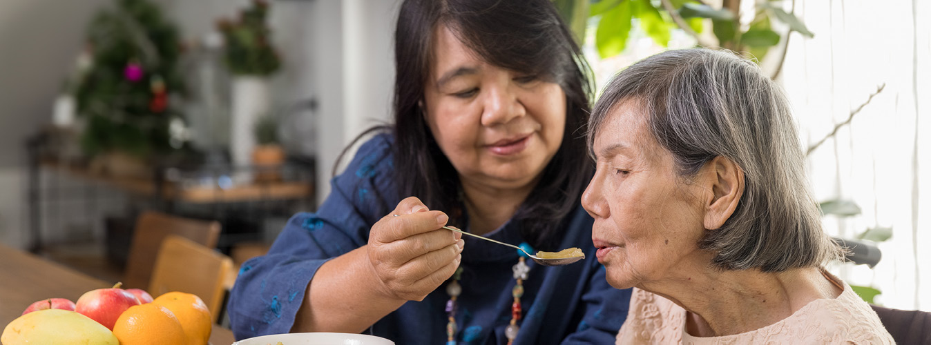 Woman spoon-feeding food to an elderly woman