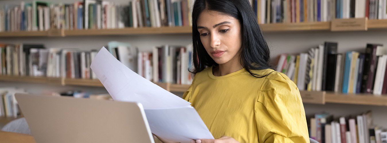 Female looking at papers while on her laptop at the library